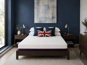 A bed with a white quilted mattress and matching white bedding, styled in a modern bedroom with a dark navy blue wall, a Union Jack accent pillow, and dark wood nightstands.
